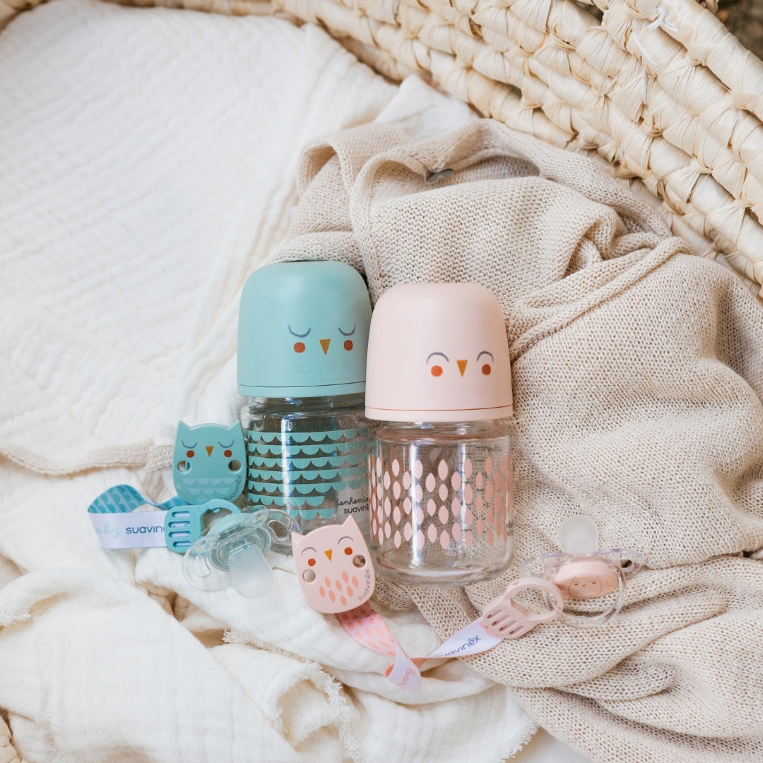 Two baby bottles with owl designs on a soft fabric background