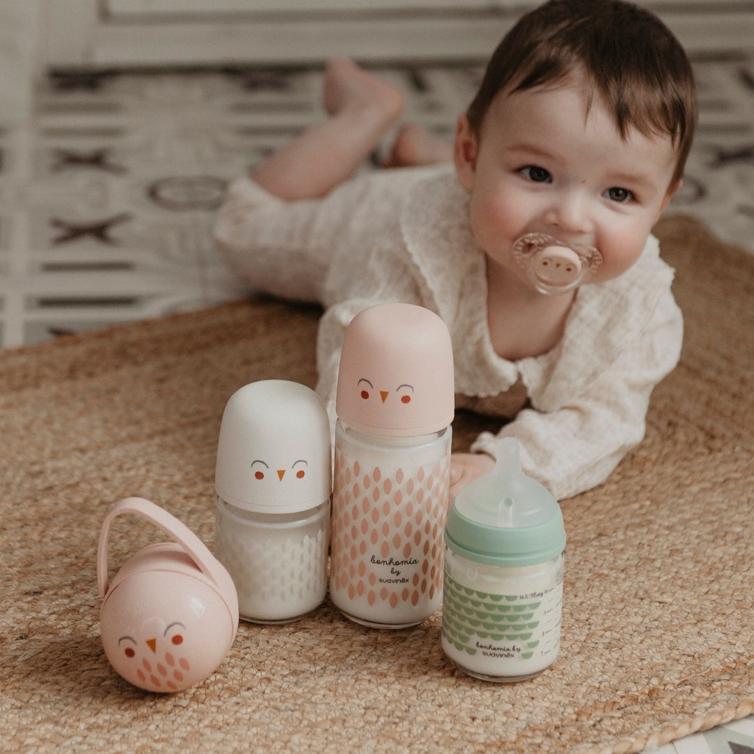 Baby lying on a blanket with colorful baby bottles around