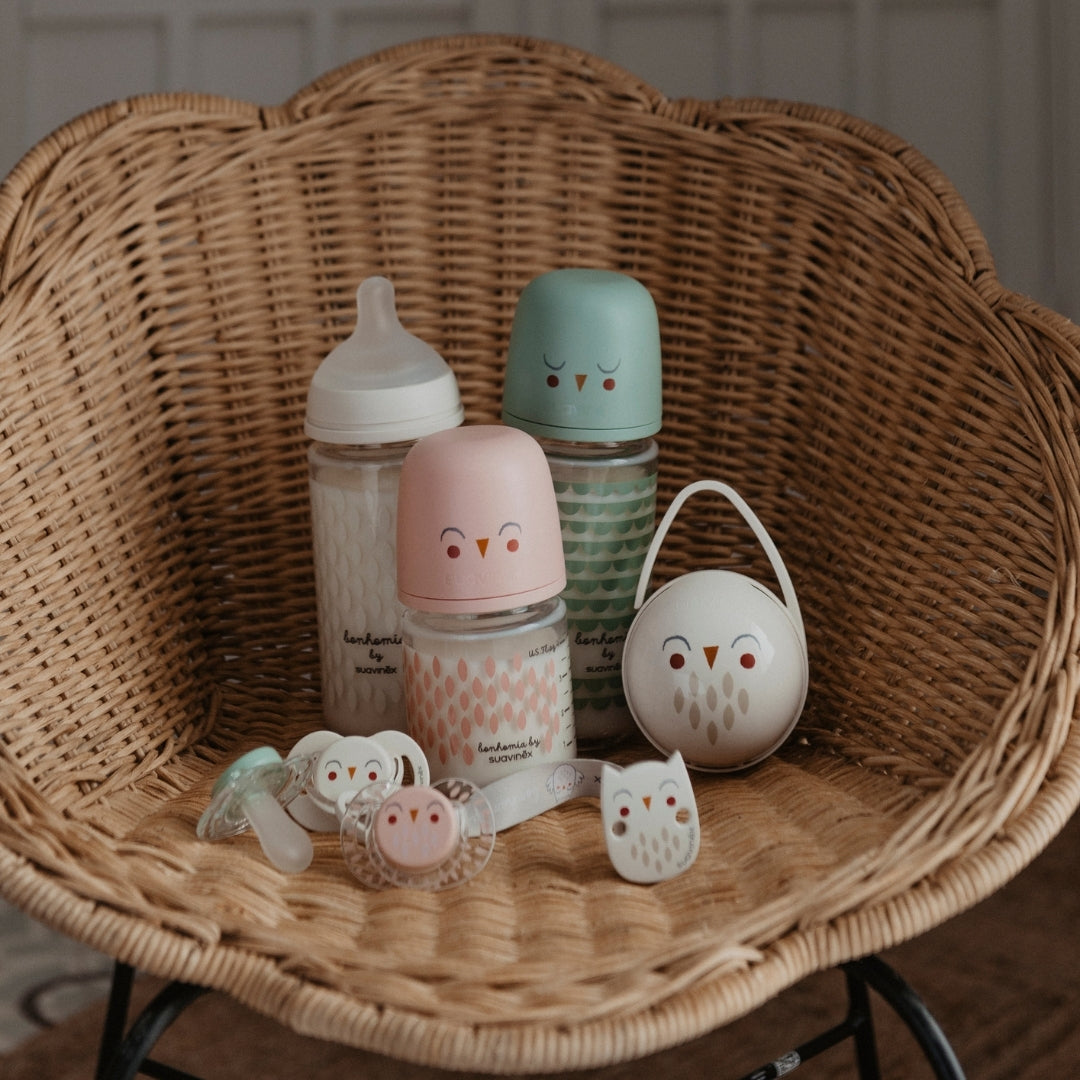 Collection of Bonhomia glass baby bottles and pacifiers on wicker chair