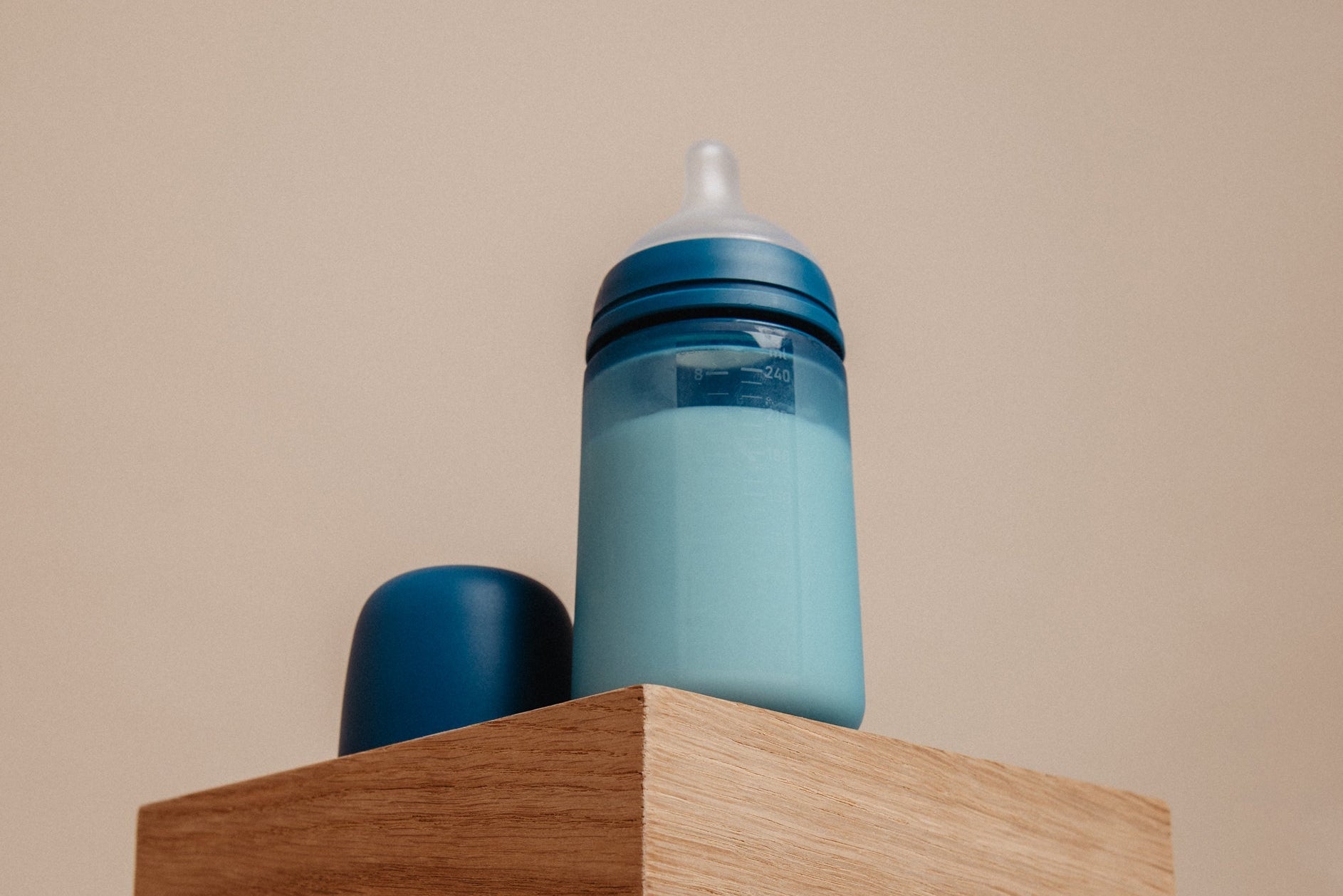 Blue bottle and pacifiers on a wooden block with a beige background